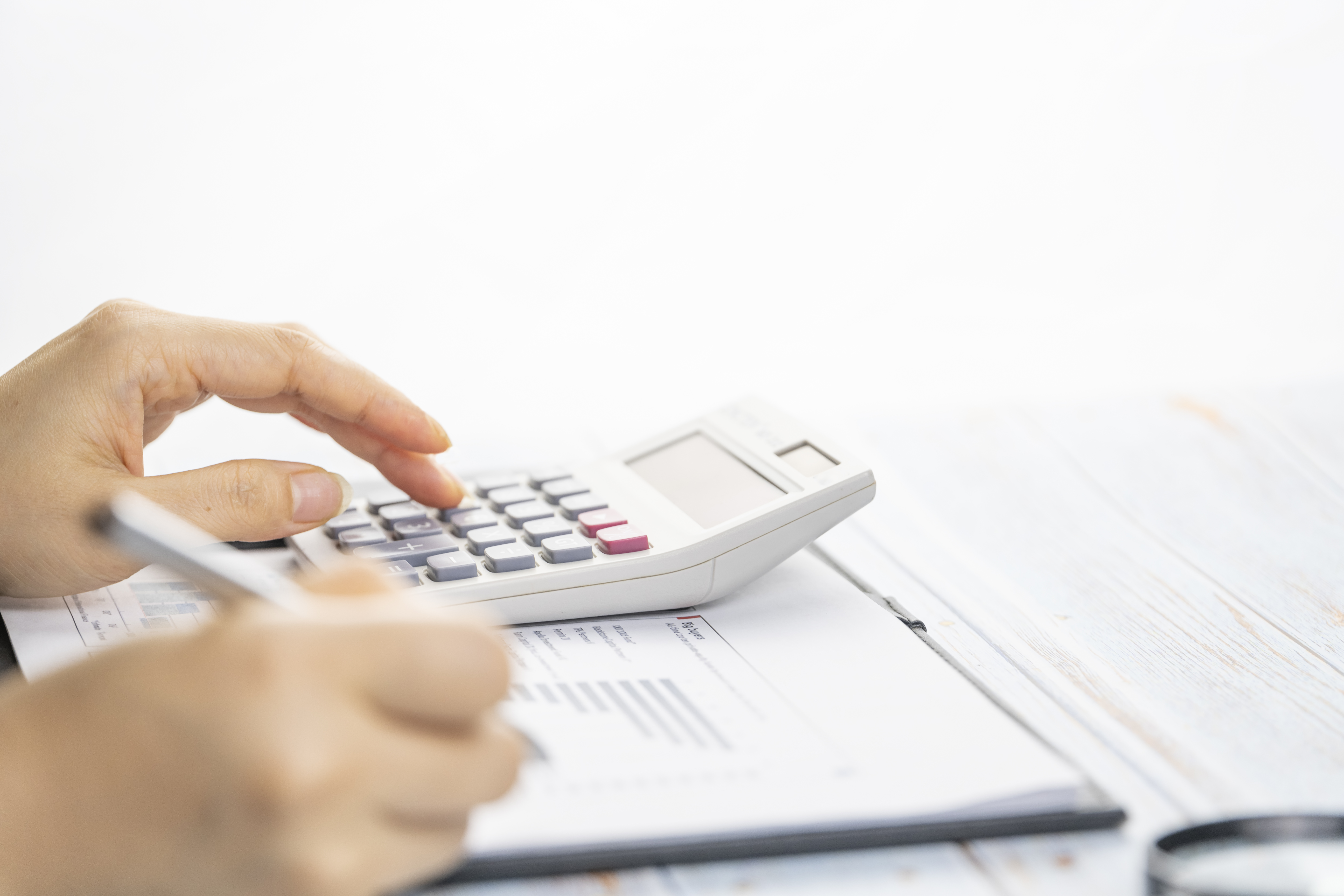 hands typing on calculator with paper at desk